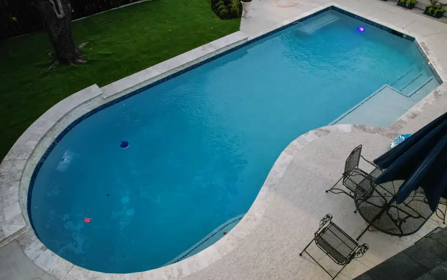Drone view of a geometric pool with a travertine deck, lawn and patio seating