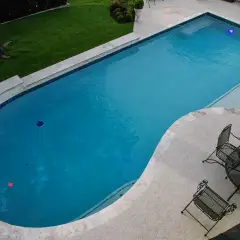 Drone view of a geometric pool with a travertine deck, lawn and patio seating