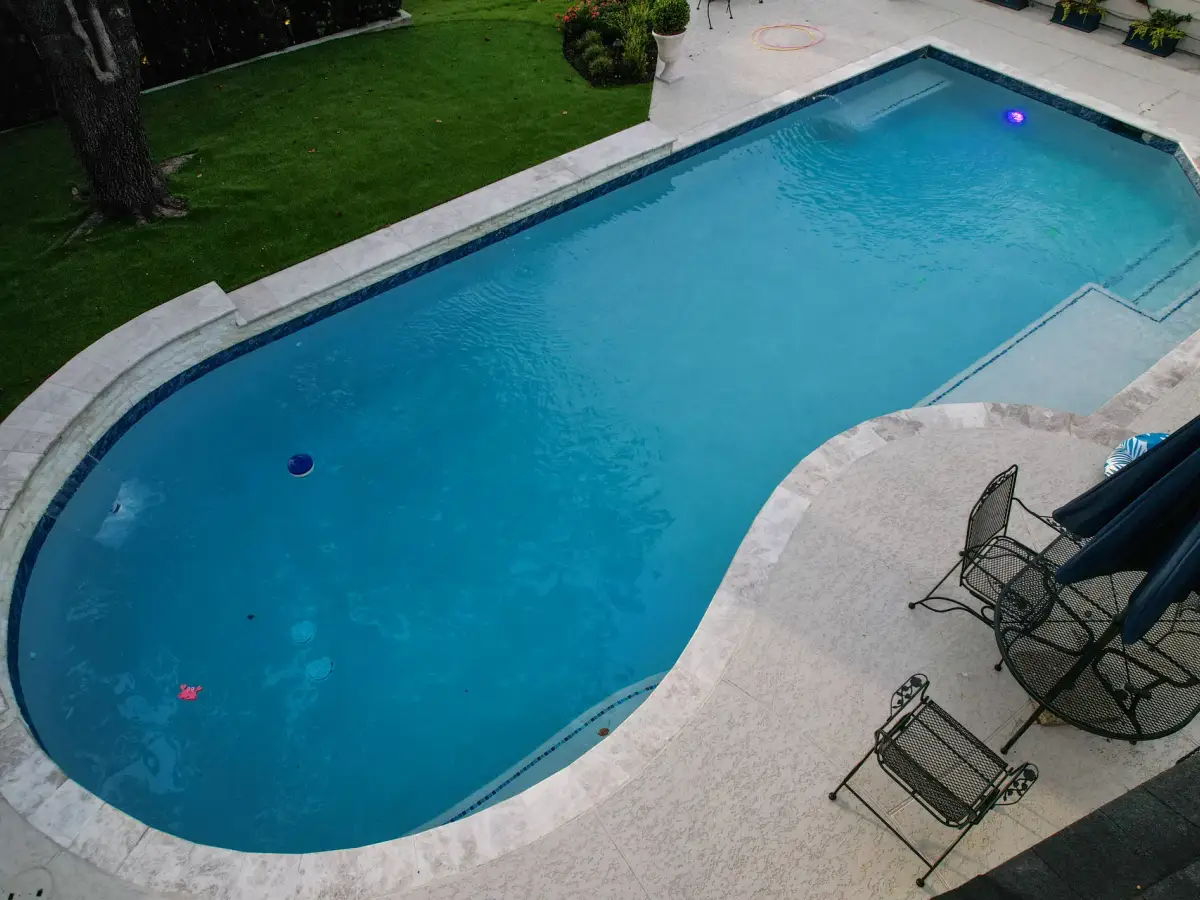 Drone view of a geometric pool with a travertine deck, lawn and patio seating