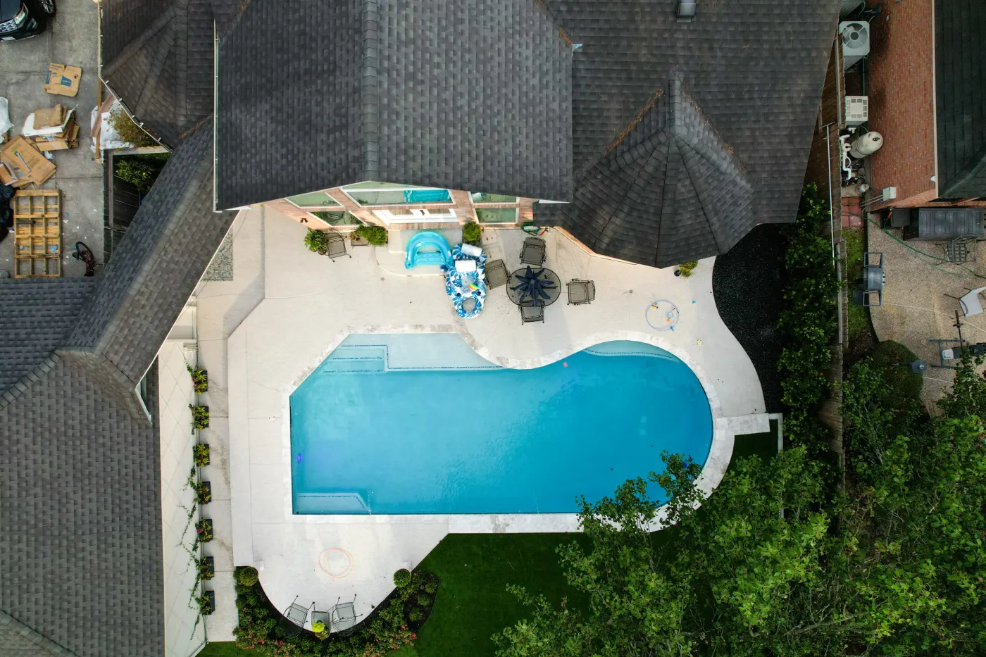 Higher drone view of the same pool showing the house roofline and garden around it