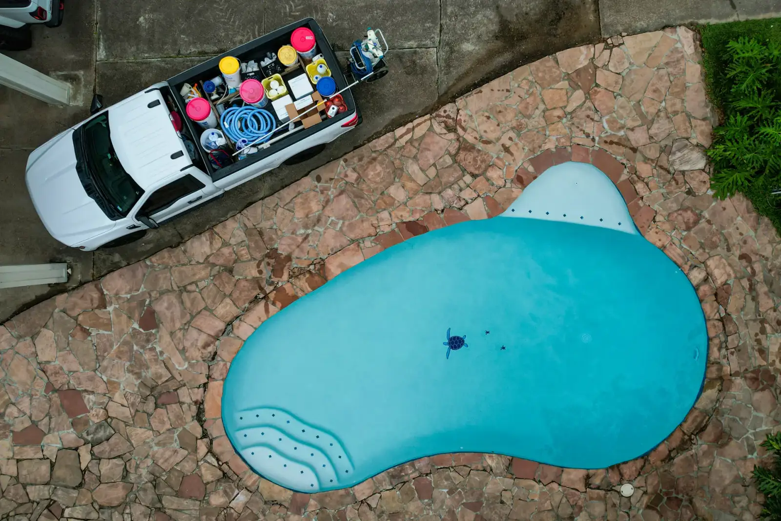 Overhead drone view of an Aloha service truck parked beside a freeform pool with a flagstone deck