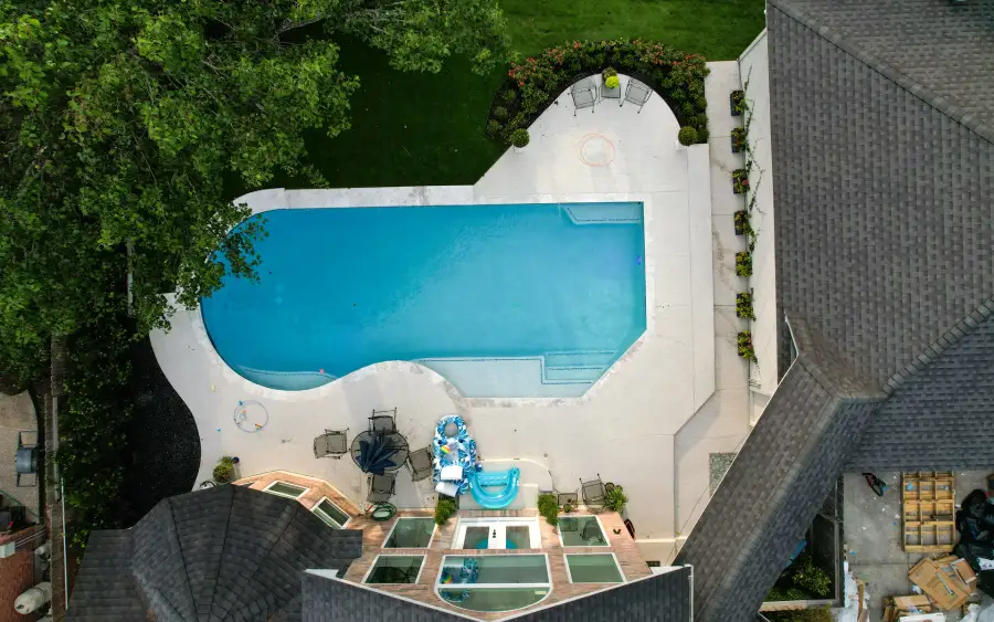 Overhead view of a rectangular pool with a curved end, white deck and seating beside the house