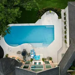 Overhead view of a rectangular pool with a curved end, white deck and seating beside the house