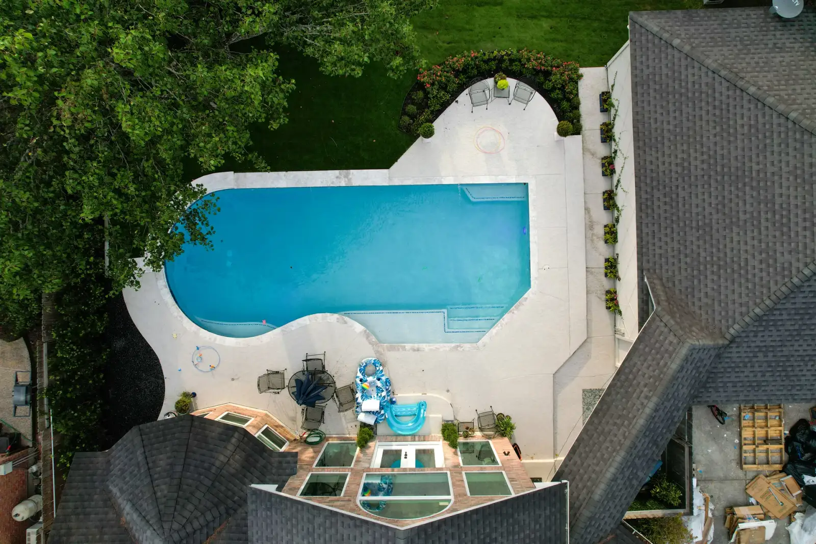 Overhead view of a rectangular pool with a curved end, white deck and seating beside the house