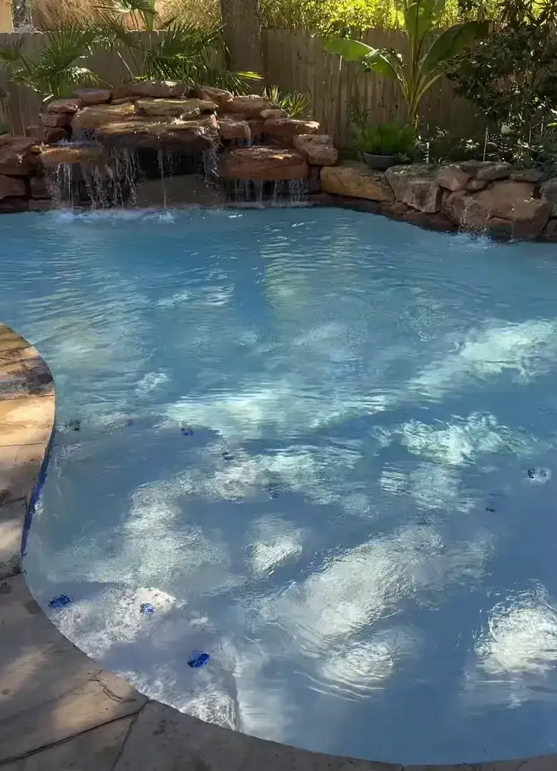 Freeform pool with clear blue water, a rock waterfall and tropical planting