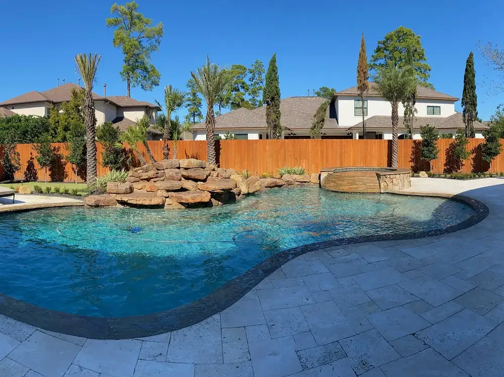 Panorama of a freeform pool with a boulder waterfall, paver deck and covered patio