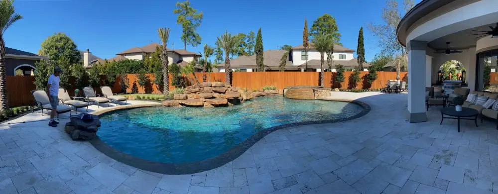 Panorama of a freeform pool with a boulder waterfall, paver deck and covered patio