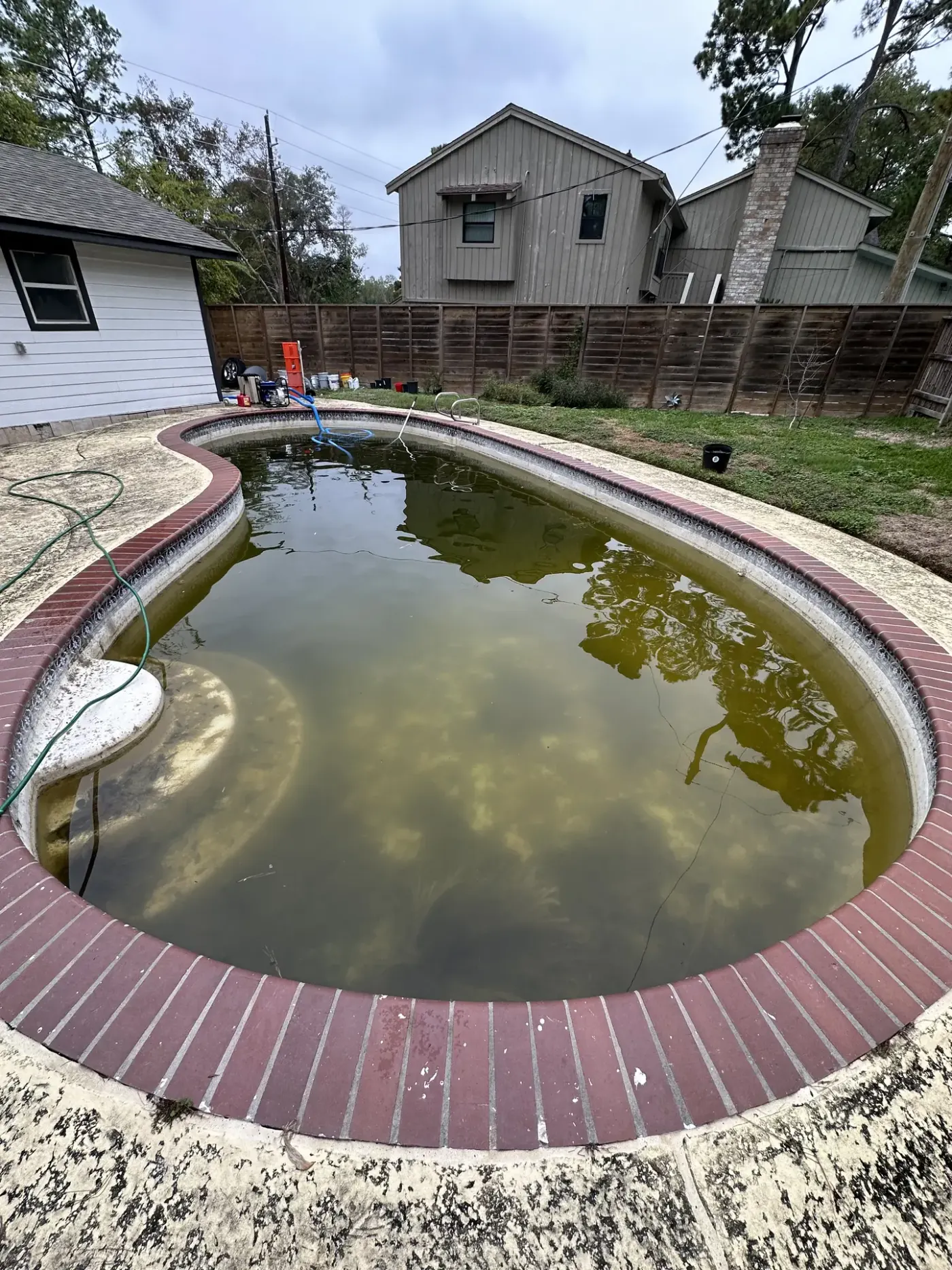 The same kidney pool before work: green, murky water inside red brick coping