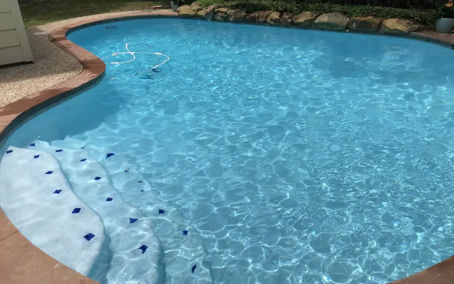 Kidney-shaped pool with white steps edged in blue diamond tiles and sunlit water