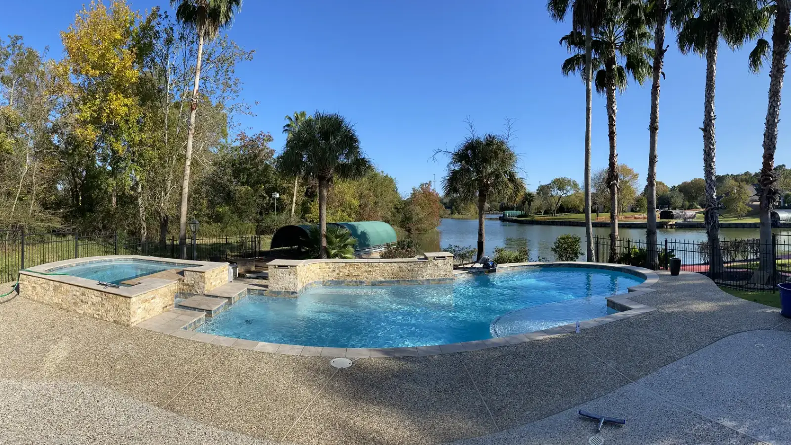 Lakeside freeform pool and raised spa with palm trees and an exposed-aggregate deck