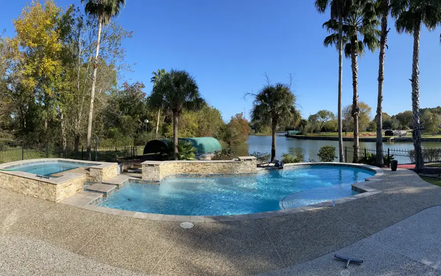Lakeside freeform pool and raised spa with palm trees and an exposed-aggregate deck