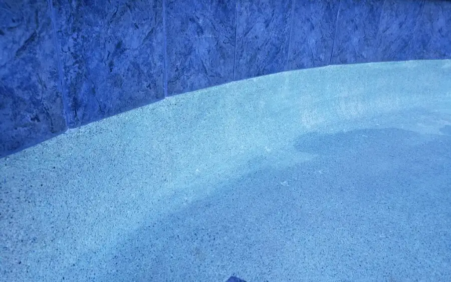 Waterline tile and speckled pebble pool finish seen close up under clear water