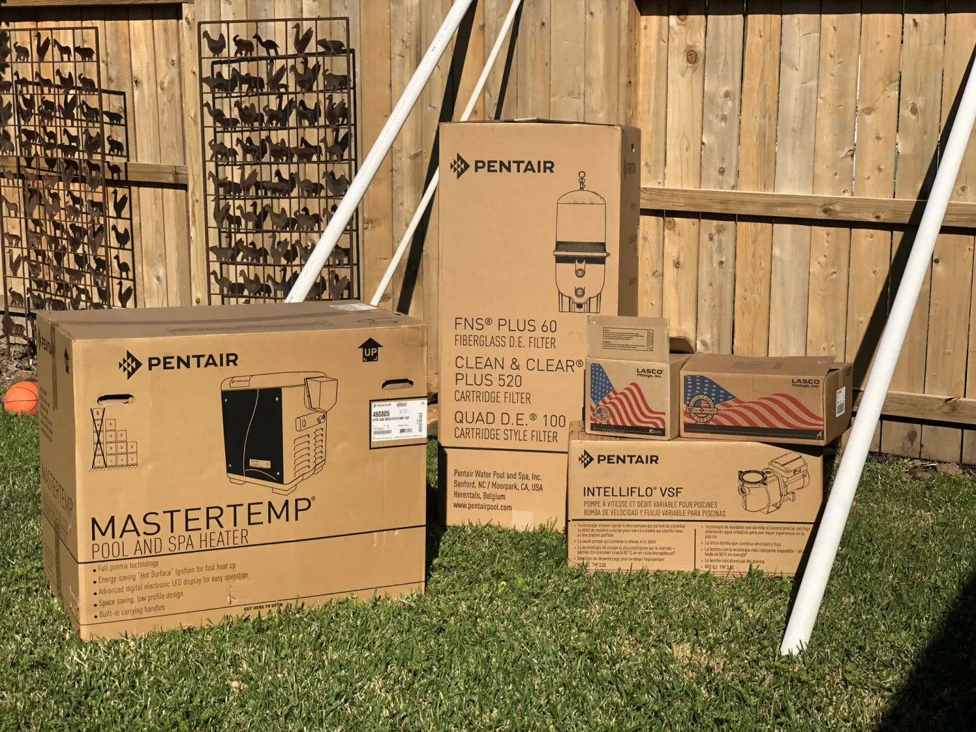Boxed Pentair MasterTemp heater, cartridge filters and IntelliFlo variable-speed pump on a lawn before installation