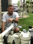 Aloha technician kneeling beside pool pump and filter plumbing during an equipment repair