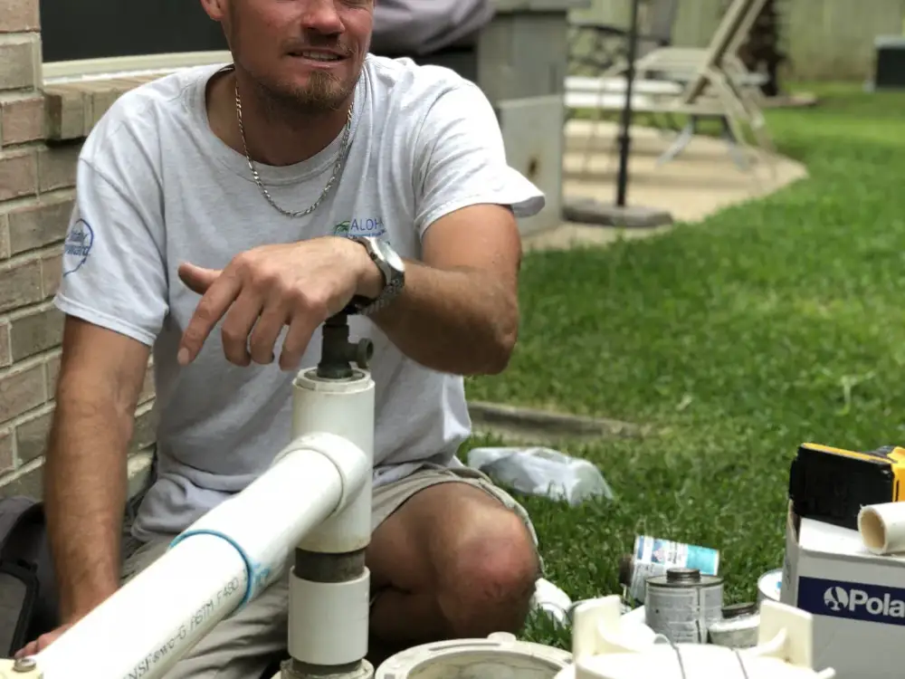 Aloha technician kneeling beside pool pump and filter plumbing during an equipment repair