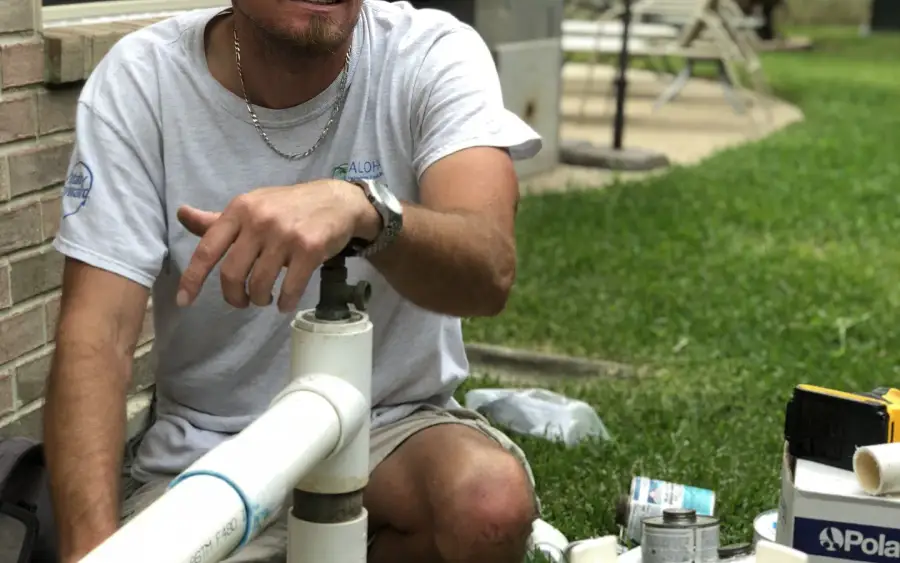 Aloha technician kneeling beside pool pump and filter plumbing during an equipment repair