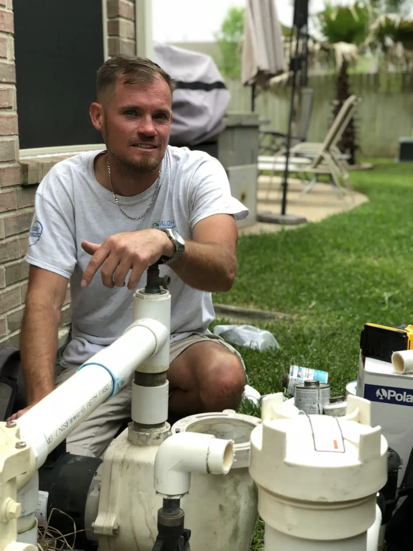 Aloha technician kneeling beside pool pump and filter plumbing during an equipment repair
