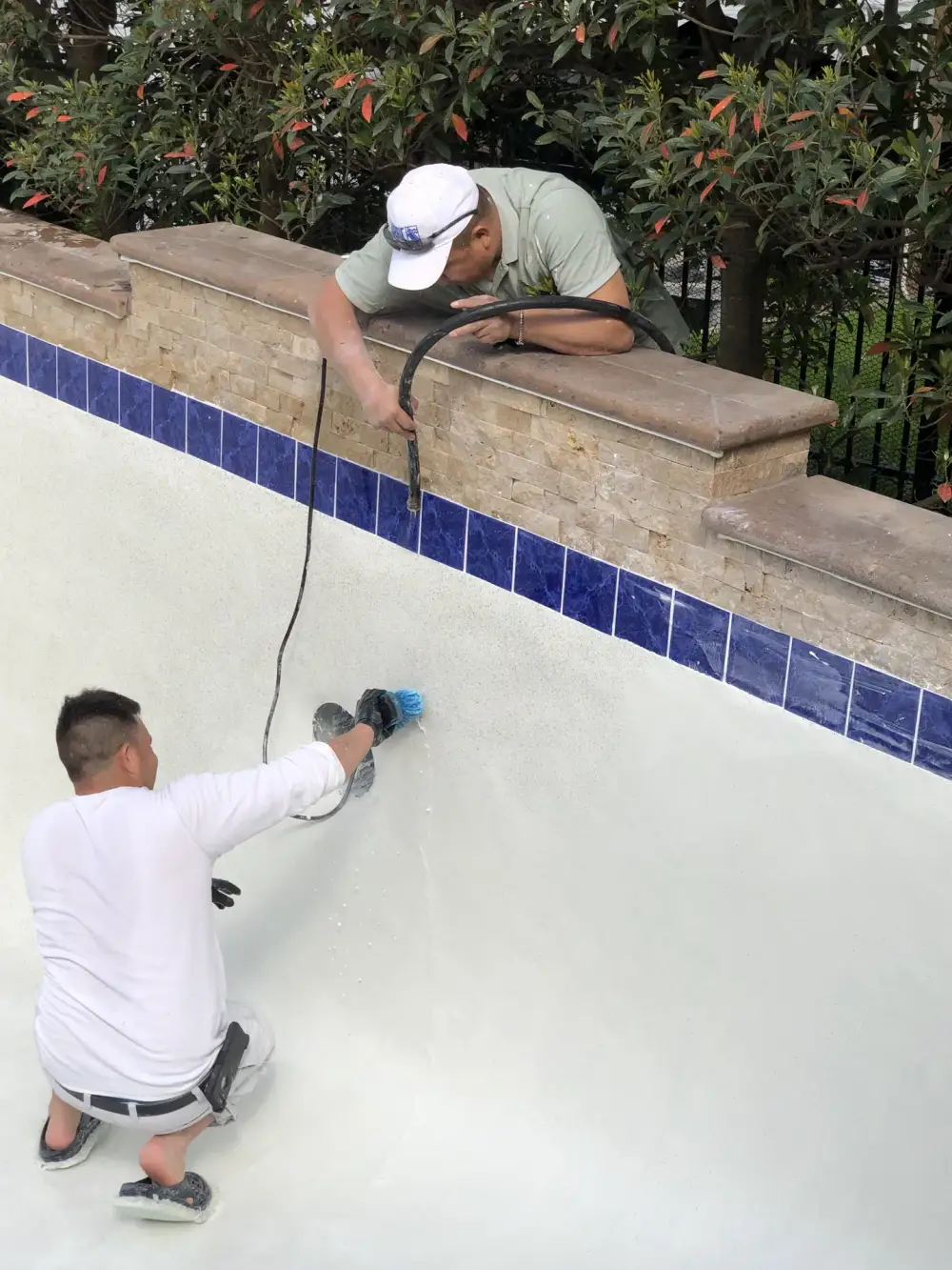 Aloha crew preparing a drained white pool shell below blue waterline tile and a stacked-stone wall