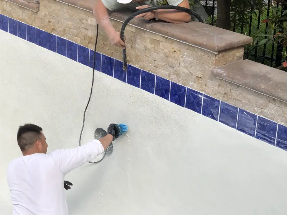 Aloha crew preparing a drained white pool shell below blue waterline tile and a stacked-stone wall