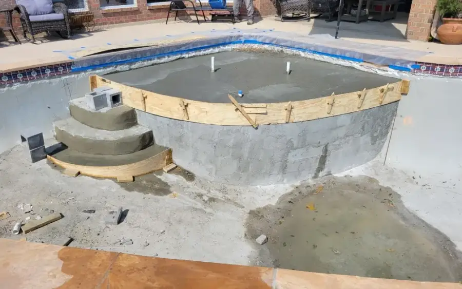 Pool mid-remodel with timber forms shaping new curved entry steps and fresh shotcrete