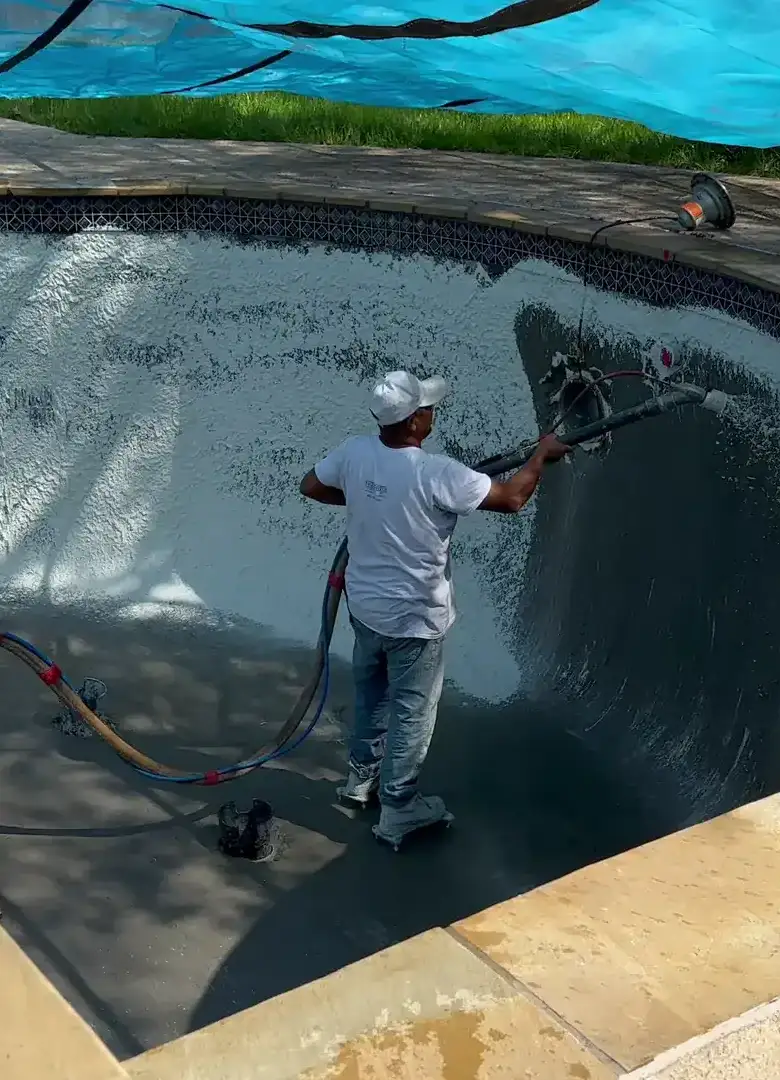 Aloha crew spraying new finish onto the walls of a drained pool under a blue shade canopy