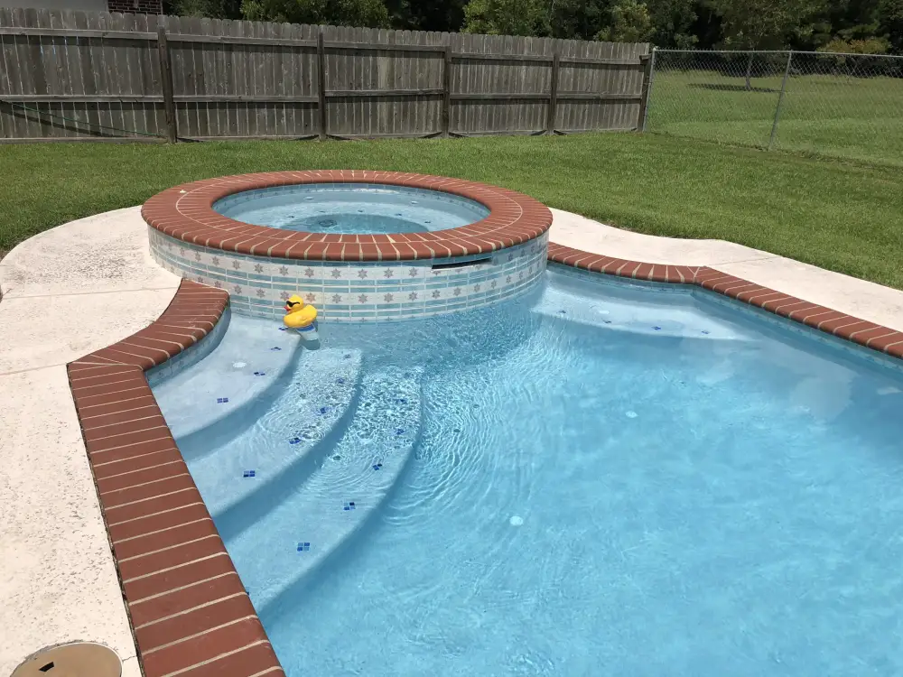 Pool with tiled entry steps and a raised round spa, both edged in red brick coping, beside a lawn