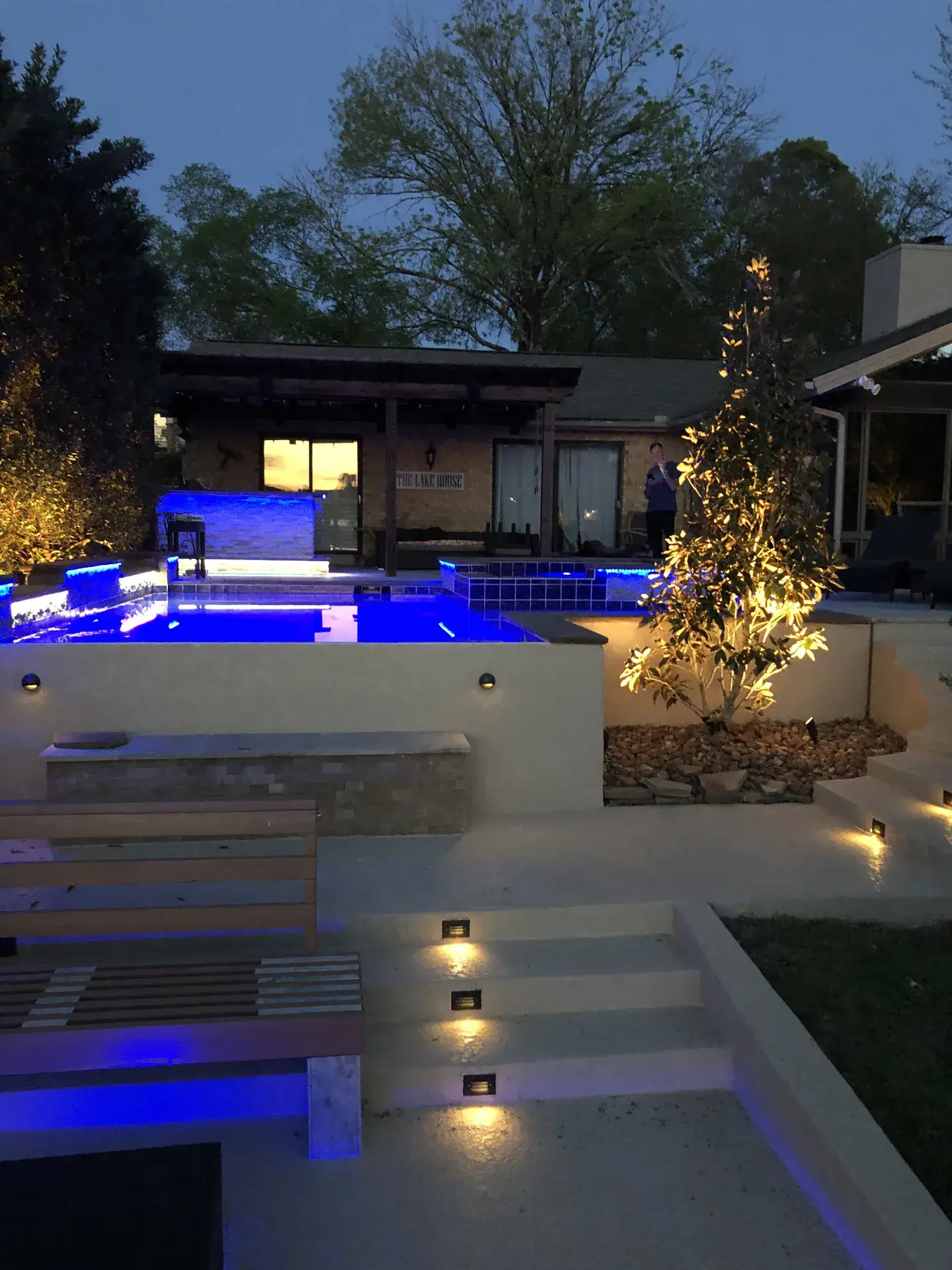 Raised spa lit blue at dusk above terrace steps with warm step lights and uplit trees