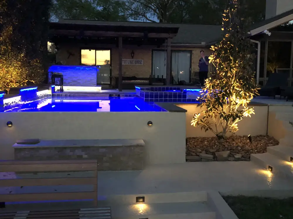 Evening view of a raised spa lit blue above lit terrace steps, with uplit trees behind