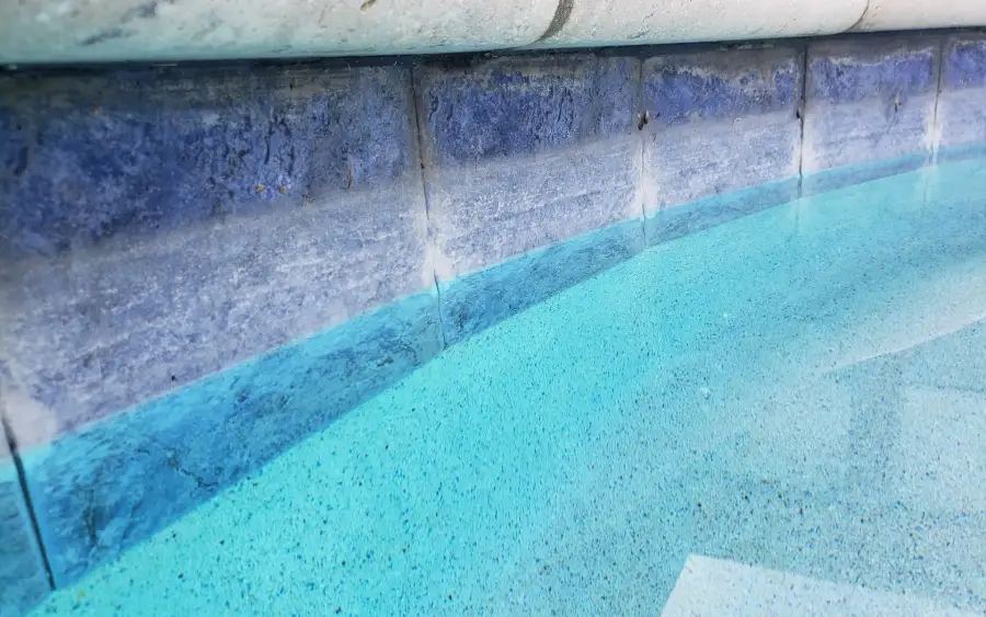 Close view of blue waterline tile under light stone coping at the edge of a pool