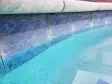 Close view of blue waterline tile under light stone coping at the edge of a pool