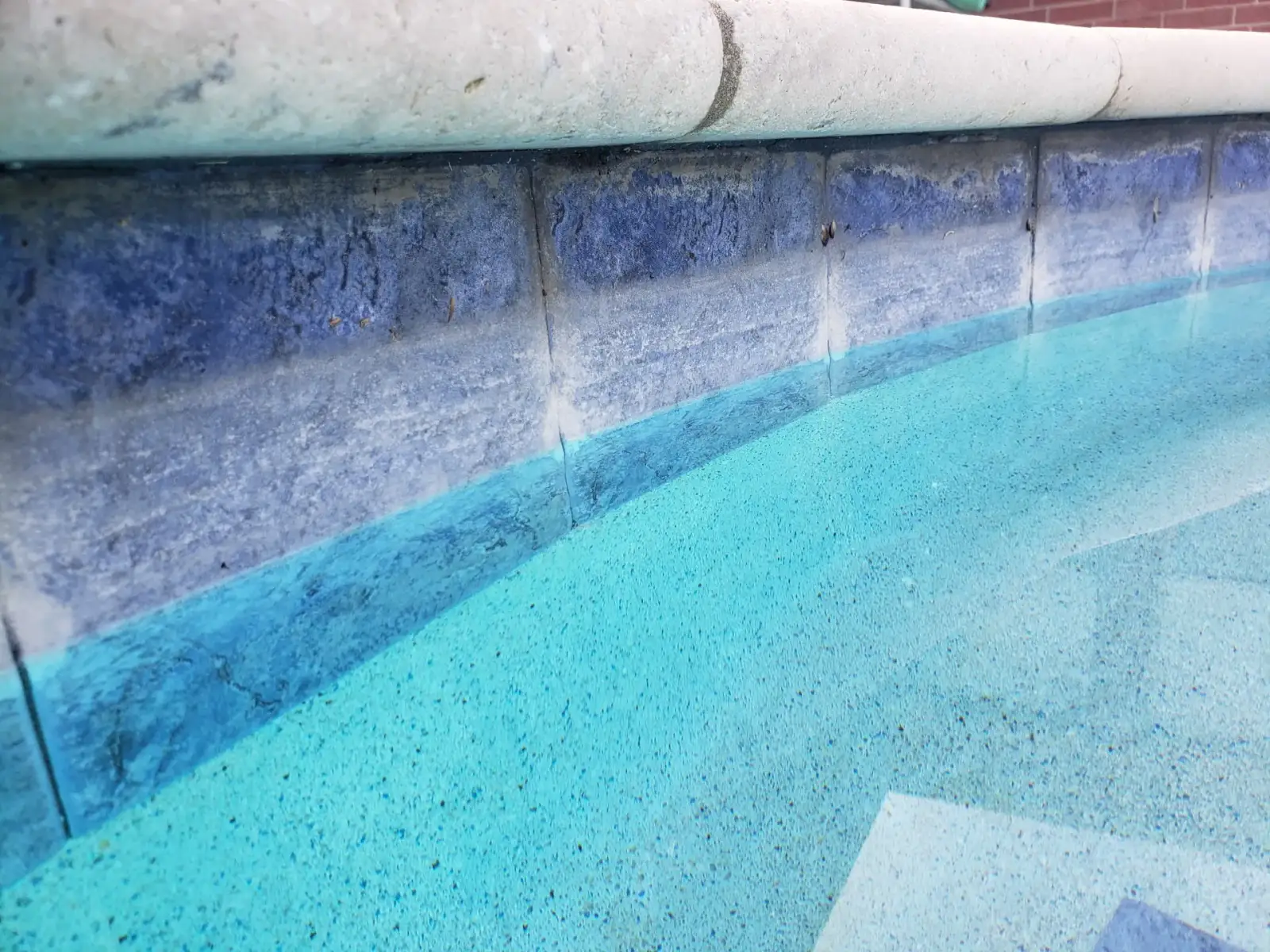 Close view of blue waterline tile under light stone coping at the edge of a pool