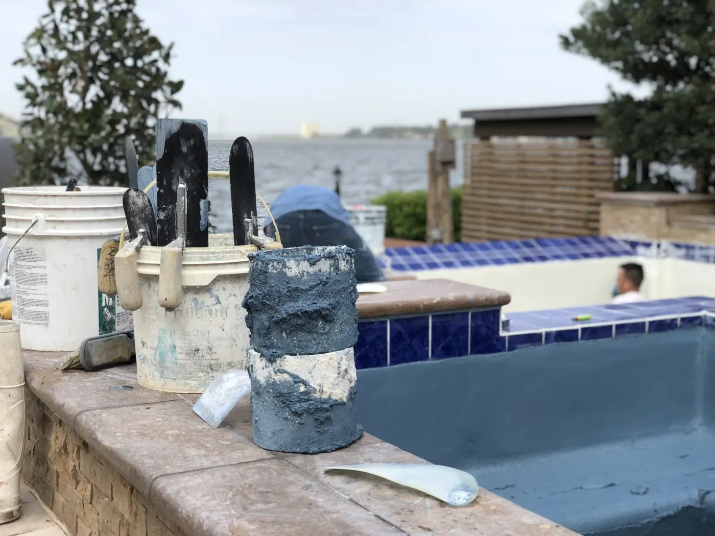 Plastering trowels and buckets on the spa coping with the drained spa and lake behind