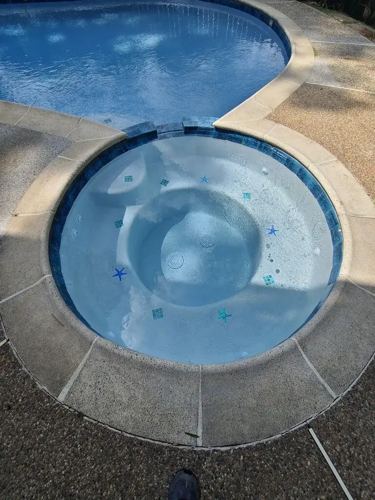 Round spa with starfish tiles in white plaster, set into an exposed-aggregate deck