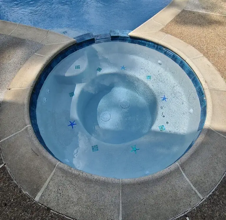 Round spa with starfish tiles in white plaster, set into an exposed-aggregate deck