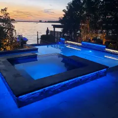 Raised spa lit blue at dusk with lake water and trees behind