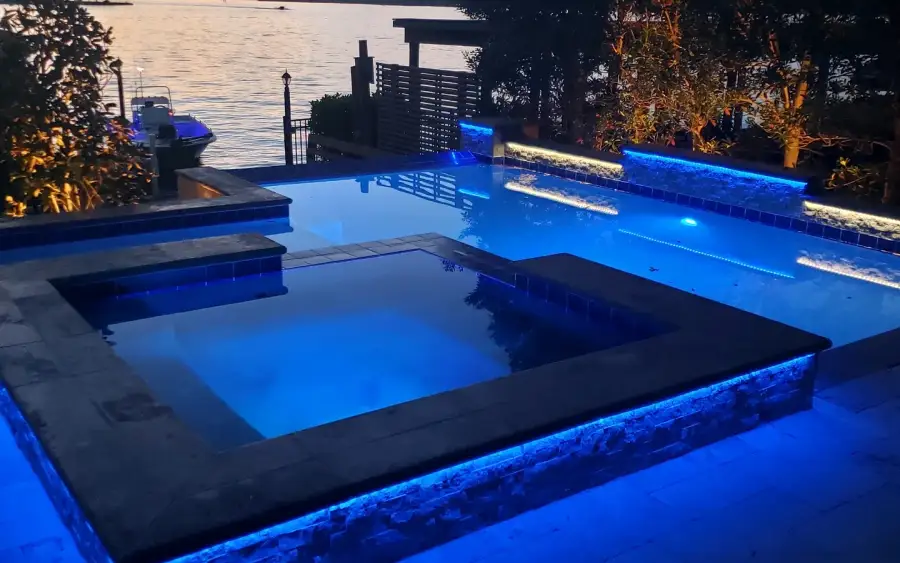 Raised spa lit blue at dusk with lake water and trees behind