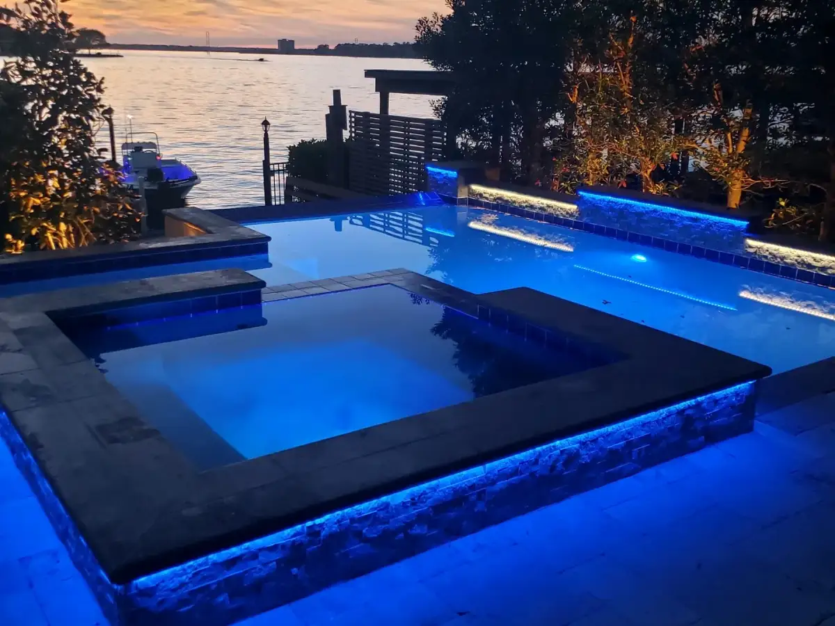 Raised spa lit blue at dusk with lake water and trees behind