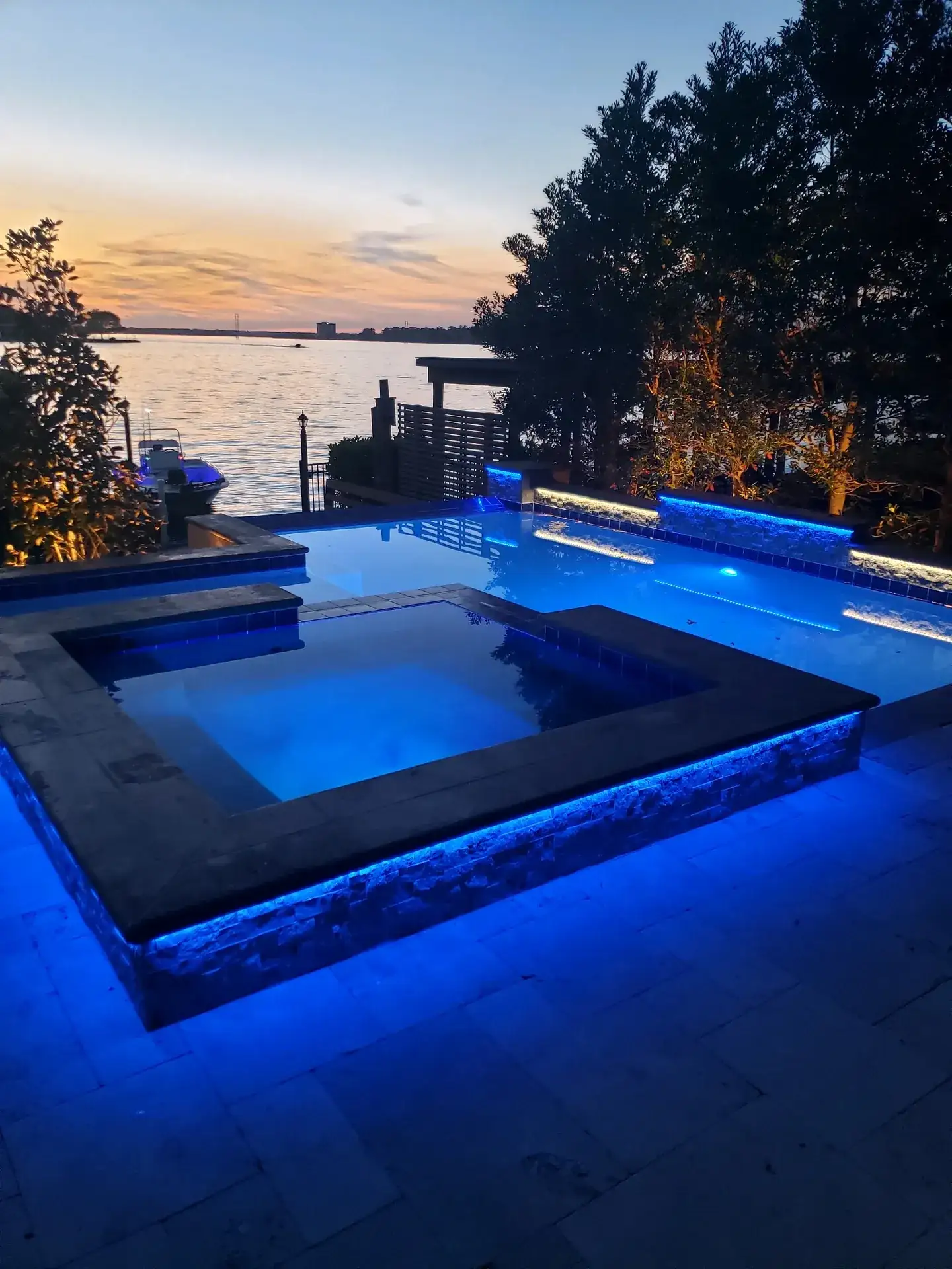 Raised spa lit blue at dusk with lake water and trees behind