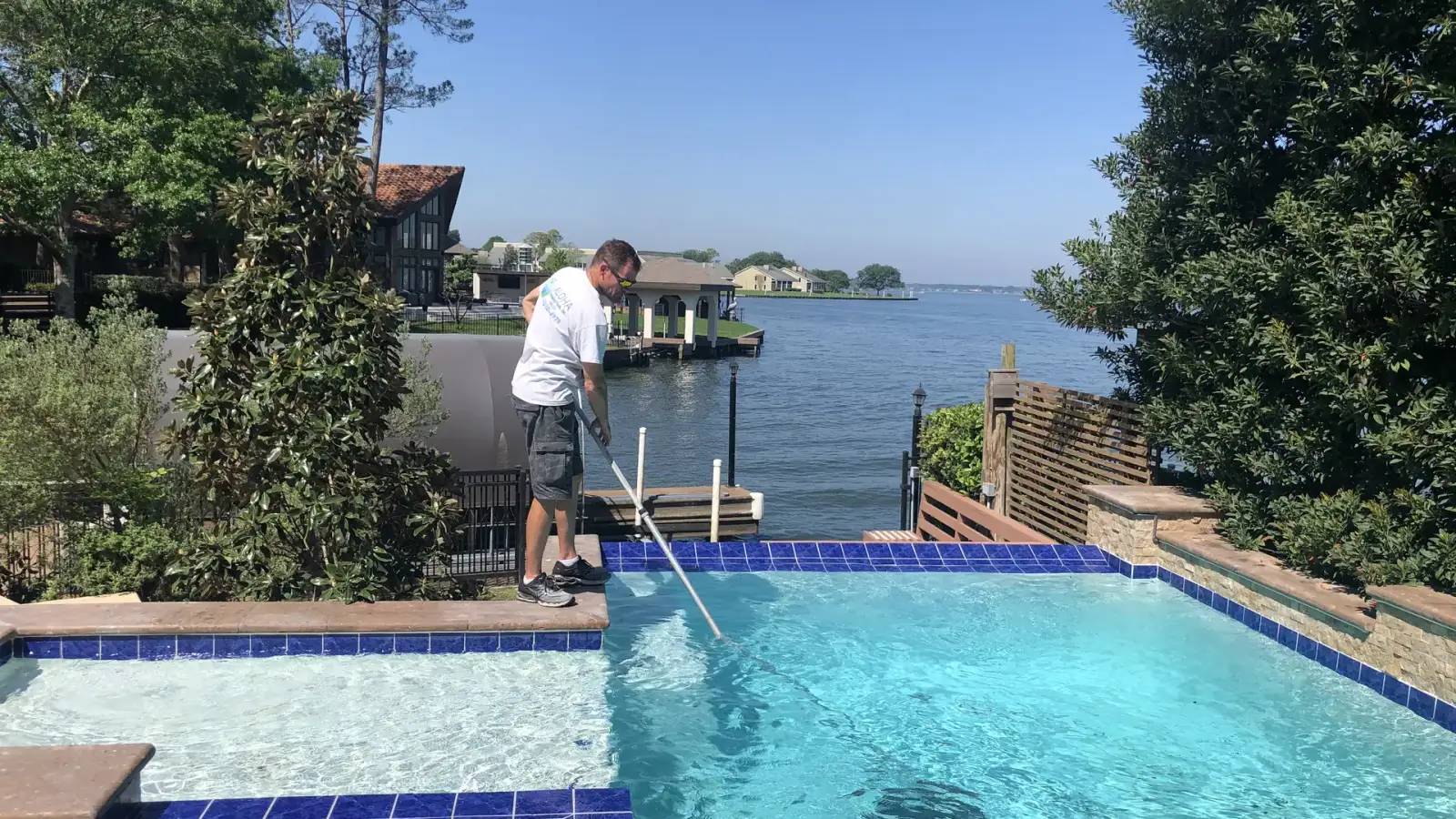 Aloha technician cleaning a waterfront pool with blue waterline tile using a telescopic pole