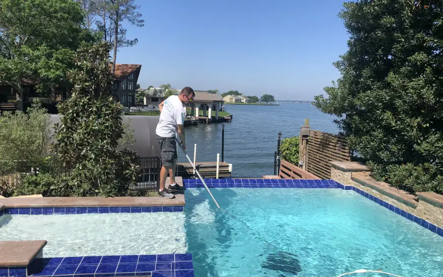 Aloha technician cleaning a waterfront pool with blue waterline tile using a telescopic pole
