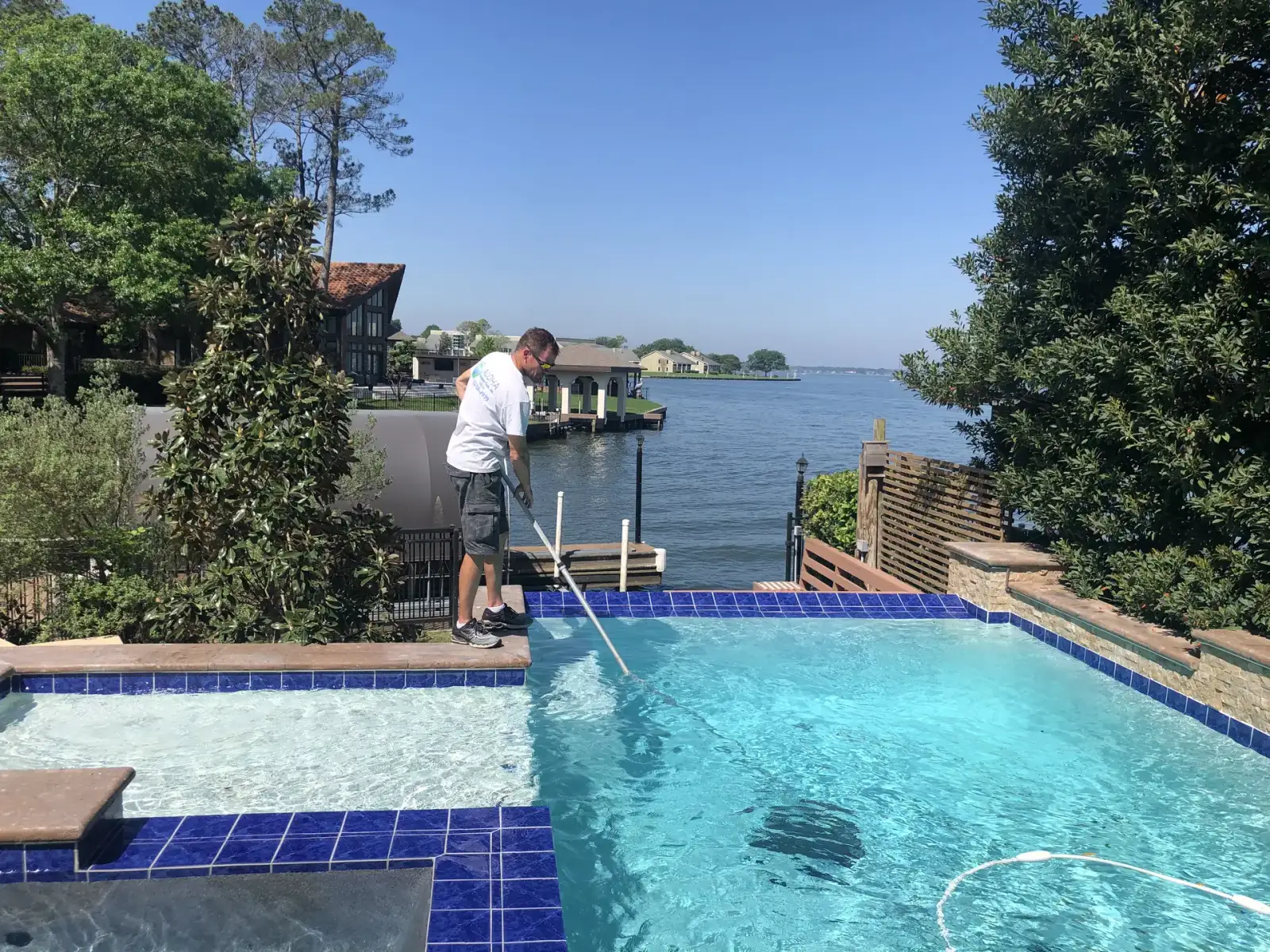 Aloha technician cleaning a waterfront pool with blue waterline tile using a telescopic pole